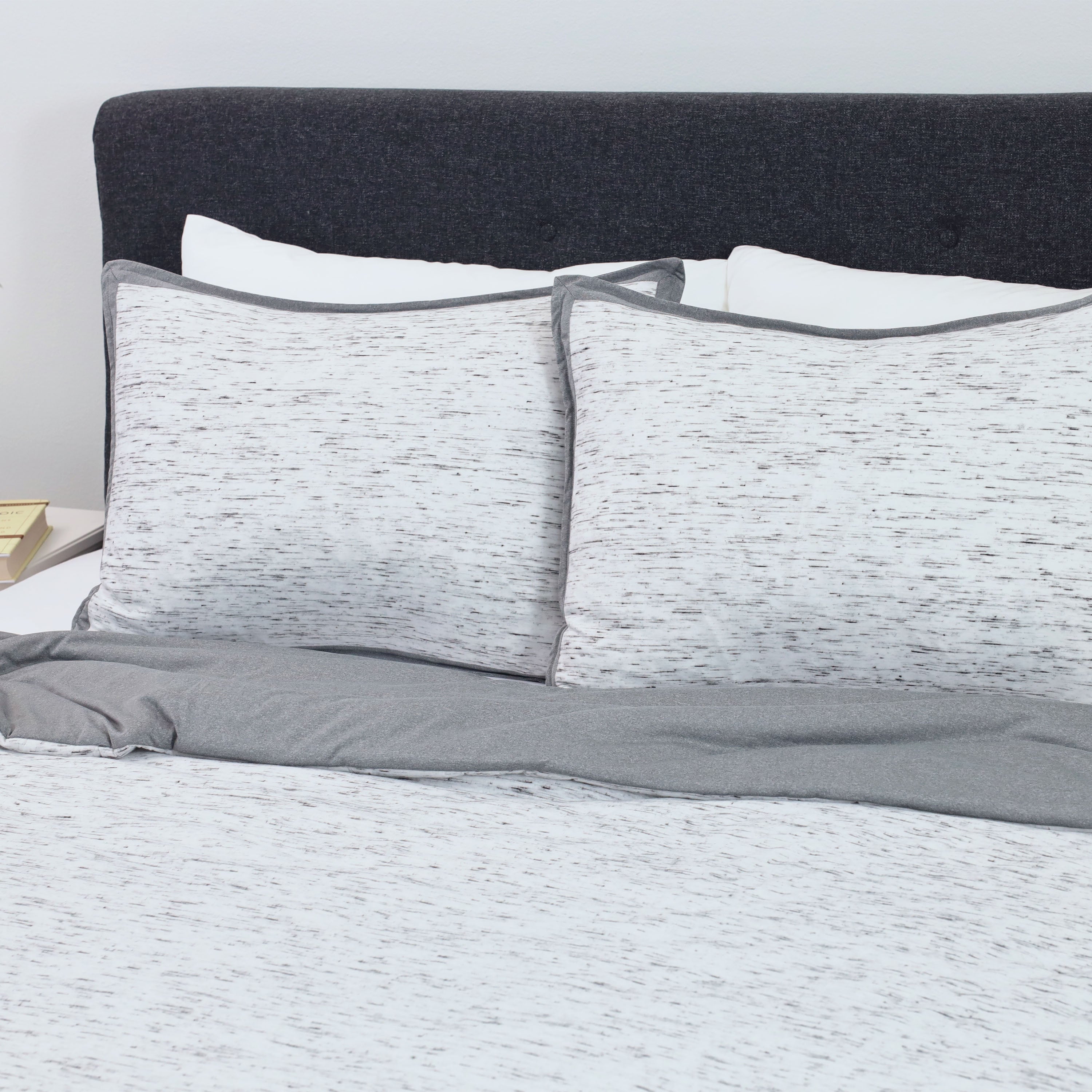 Comforter set featuring a textured white and gray design with matching pillow shams on a bed with a dark headboard.