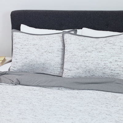 Comforter set featuring a textured white and gray design with matching pillow shams on a bed with a dark headboard.