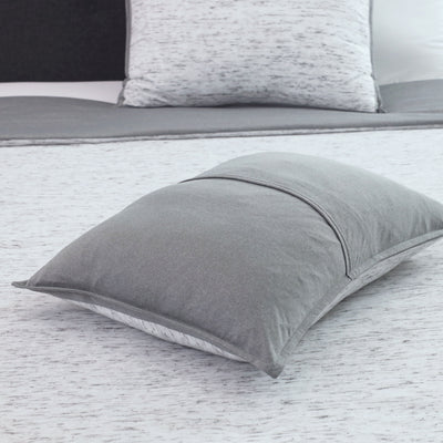 Gray decorative pillow with a smooth texture, resting on a light-colored bedspread.