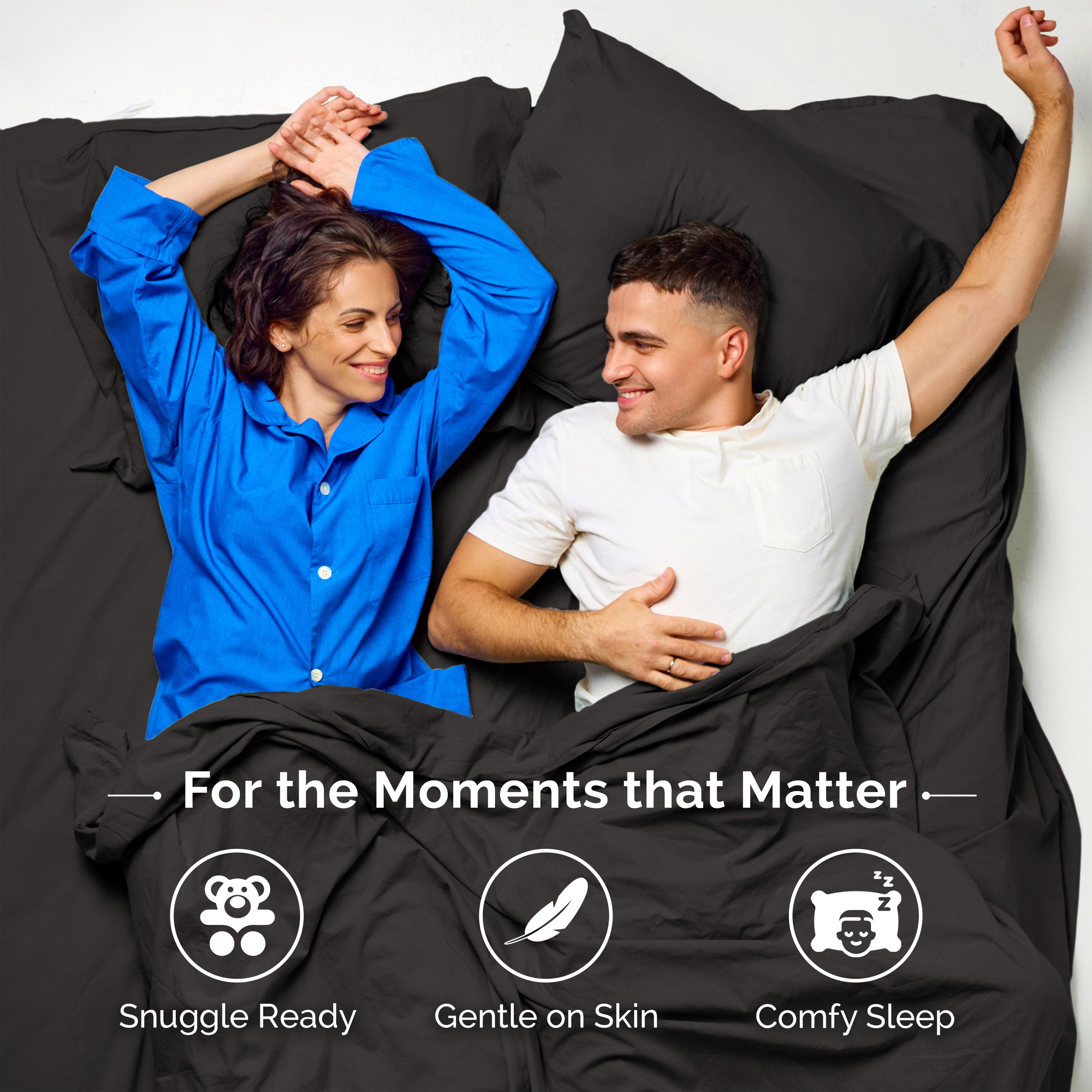 Couple lying on black sheets, smiling and relaxed, with one wearing a blue shirt and the other in a white shirt.