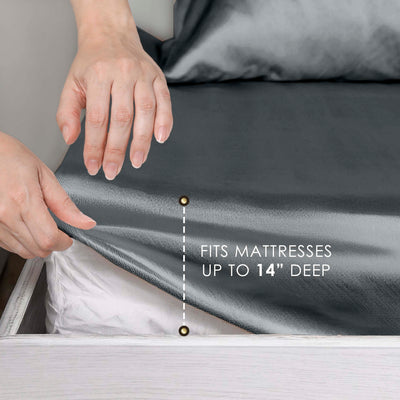 Hands adjusting a dark satin sheet on a mattress, with a note indicating it fits mattresses up to 14 inches deep.