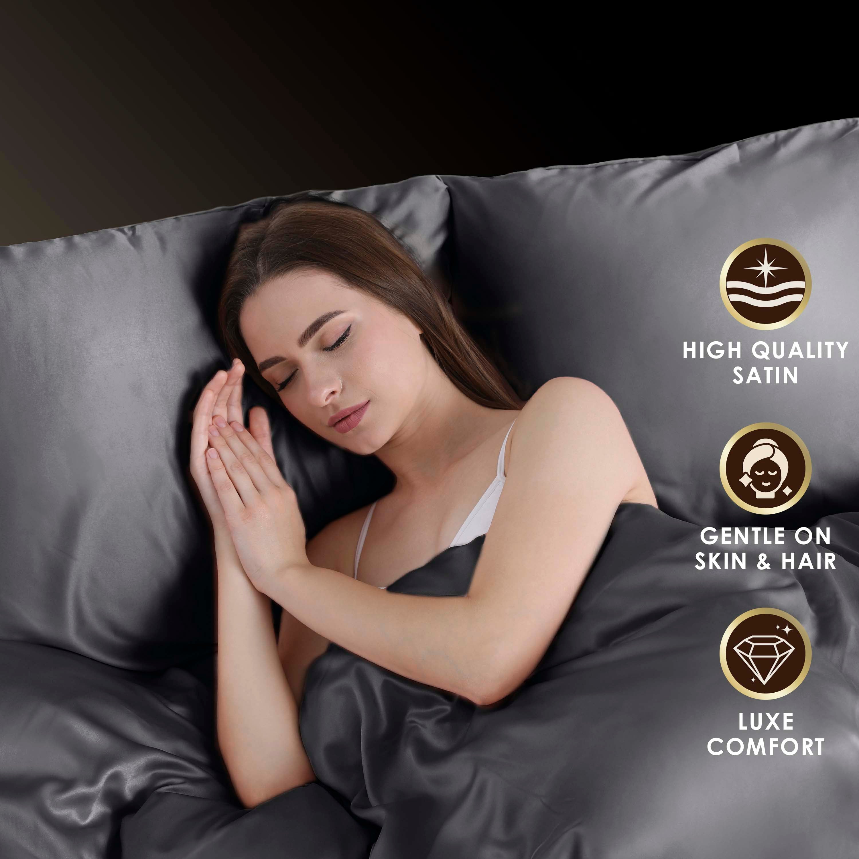 A person sleeps peacefully on dark satin sheets, with their hands clasped near their face.