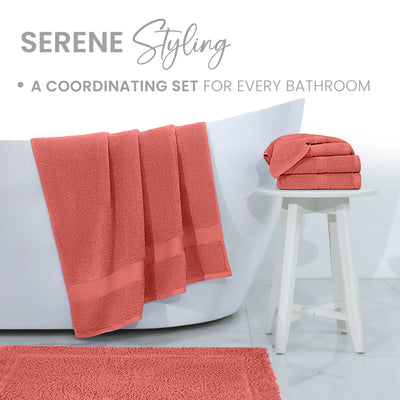 Coral bath rug with matching towels draped over a white bathtub and stacked on a small white stool.