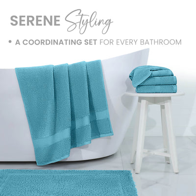 Turquoise bath towels and rug displayed near a white bathtub and a small white stool.
