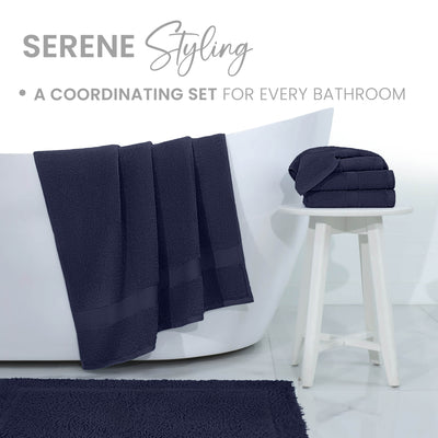 Navy bath rug displayed in a bathroom setting with towels hanging over a tub and stacked on a white stool.