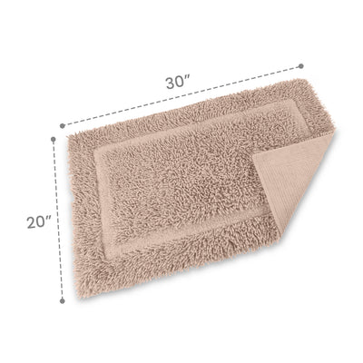 Rectangular bath rug in a light beige color, measuring 30 inches by 20 inches, with a textured surface and a folded corner.