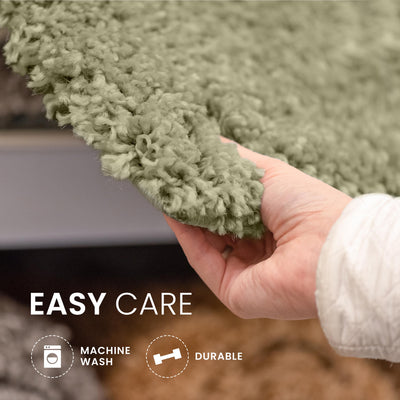 Hand holding a soft, textured green bath rug with a blurred background.