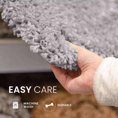 Hand holding a soft, gray bath rug with a textured surface, showcasing its easy care features.