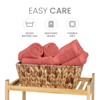 Six coral towels are neatly arranged in a woven basket on a wooden stand, with care instructions displayed above.