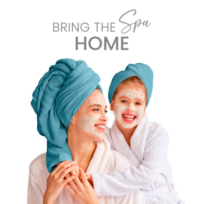 Two people with facial masks wear matching blue towels on their heads, smiling and enjoying a spa-like experience.