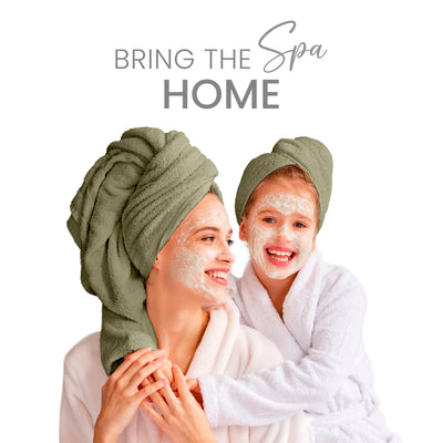 Two women, one adult and one child, wearing towels on their heads and bathrobes, smiling with facial masks on.