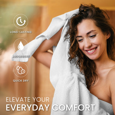 A woman with curly hair smiles while holding a white towel, with a warm background.