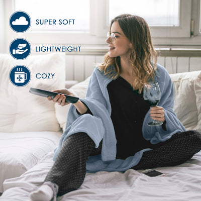 A woman sits on a bed wrapped in a light blue fleece blanket, holding a remote and a glass of wine.