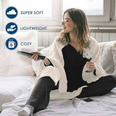 A woman sits on a bed wrapped in a white fleece blanket, holding a remote and a glass of wine.