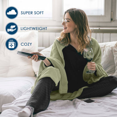A woman sits on a bed wrapped in a light green fleece blanket, holding a remote and a glass of wine.