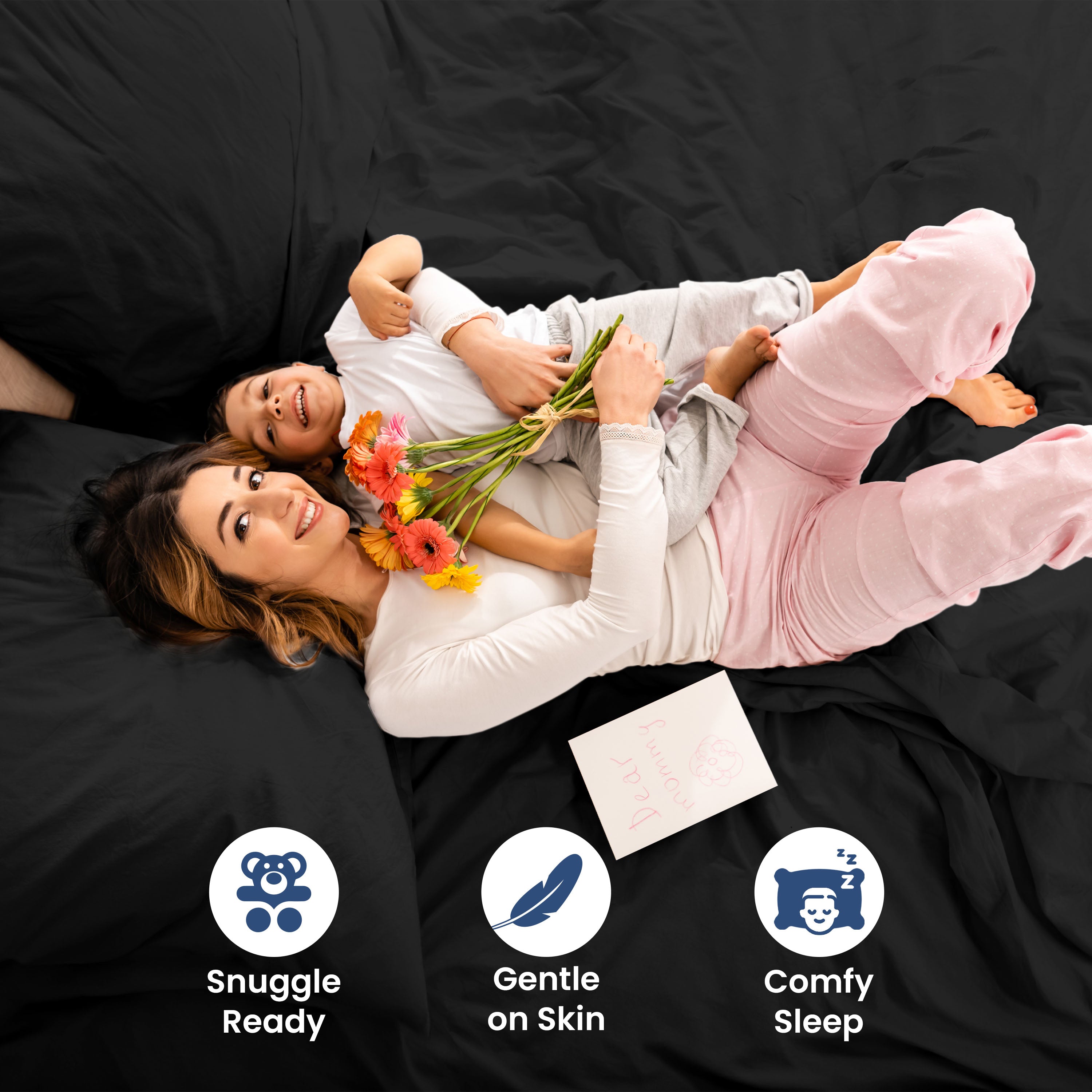 A woman and child lie on a black bedspread, holding flowers and smiling, with a card nearby.