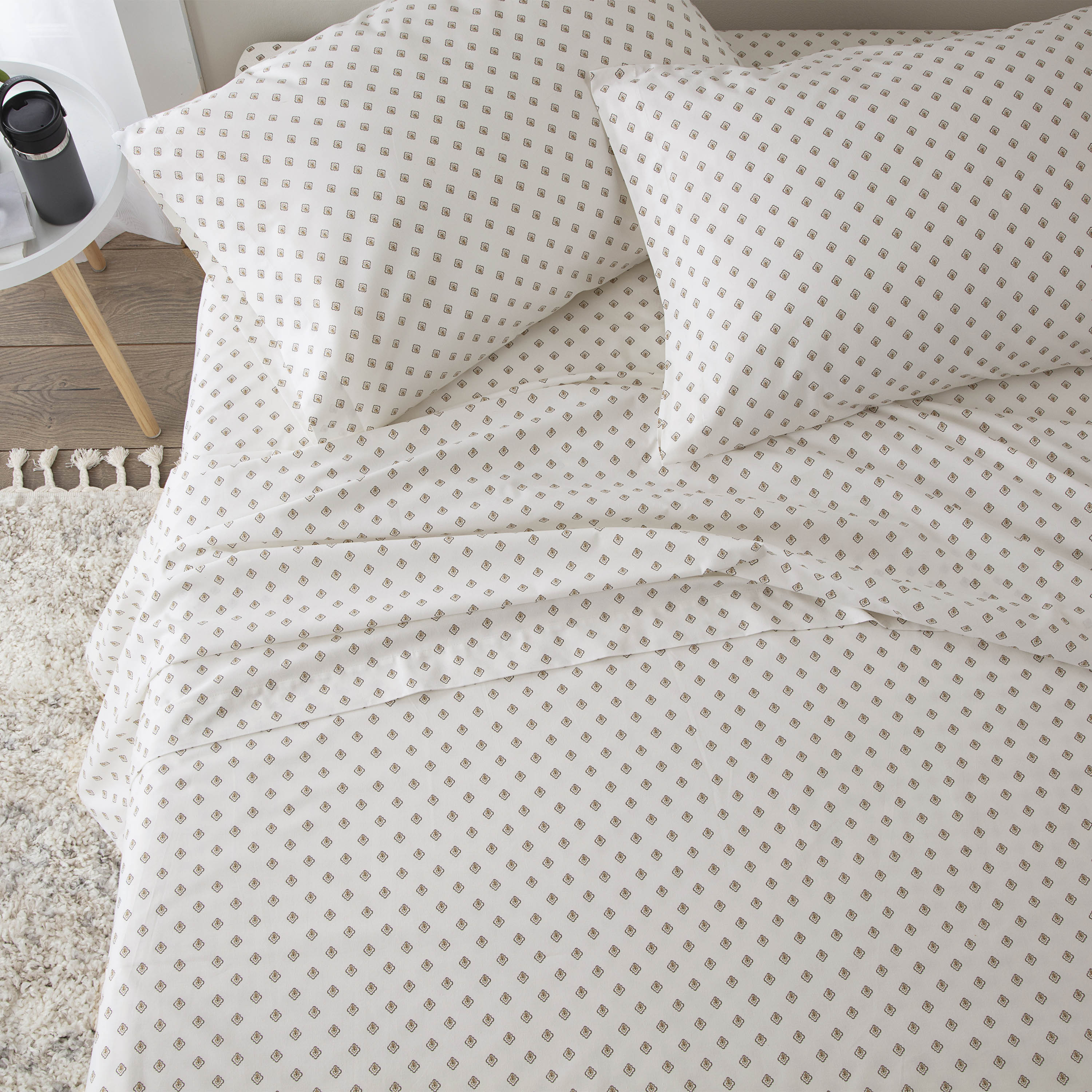 Light-colored sheet set with a geometric pattern, including two pillows and a fitted sheet on a bed.