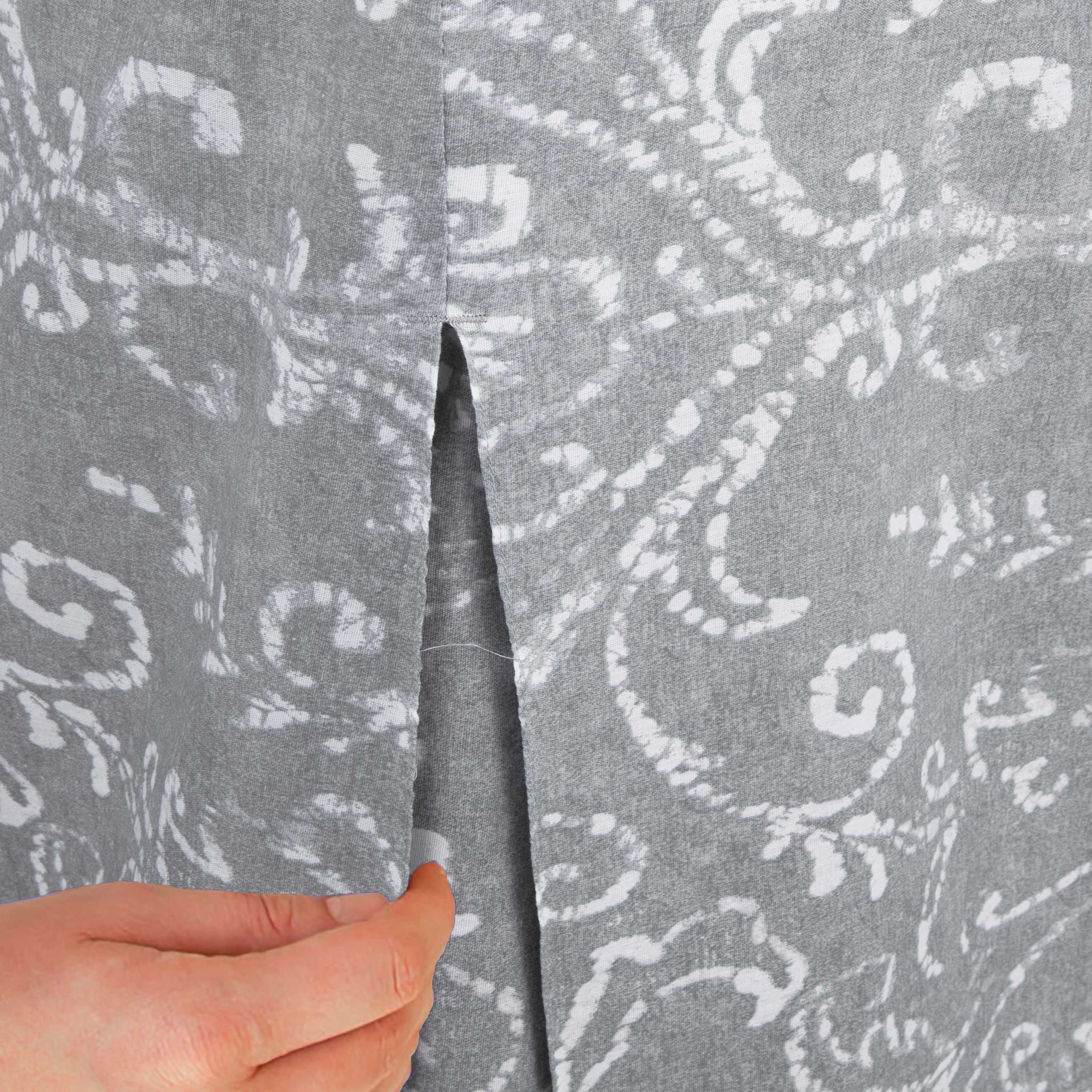Close-up of a hand holding a gray table cover with a white paisley pattern and a slit detail.