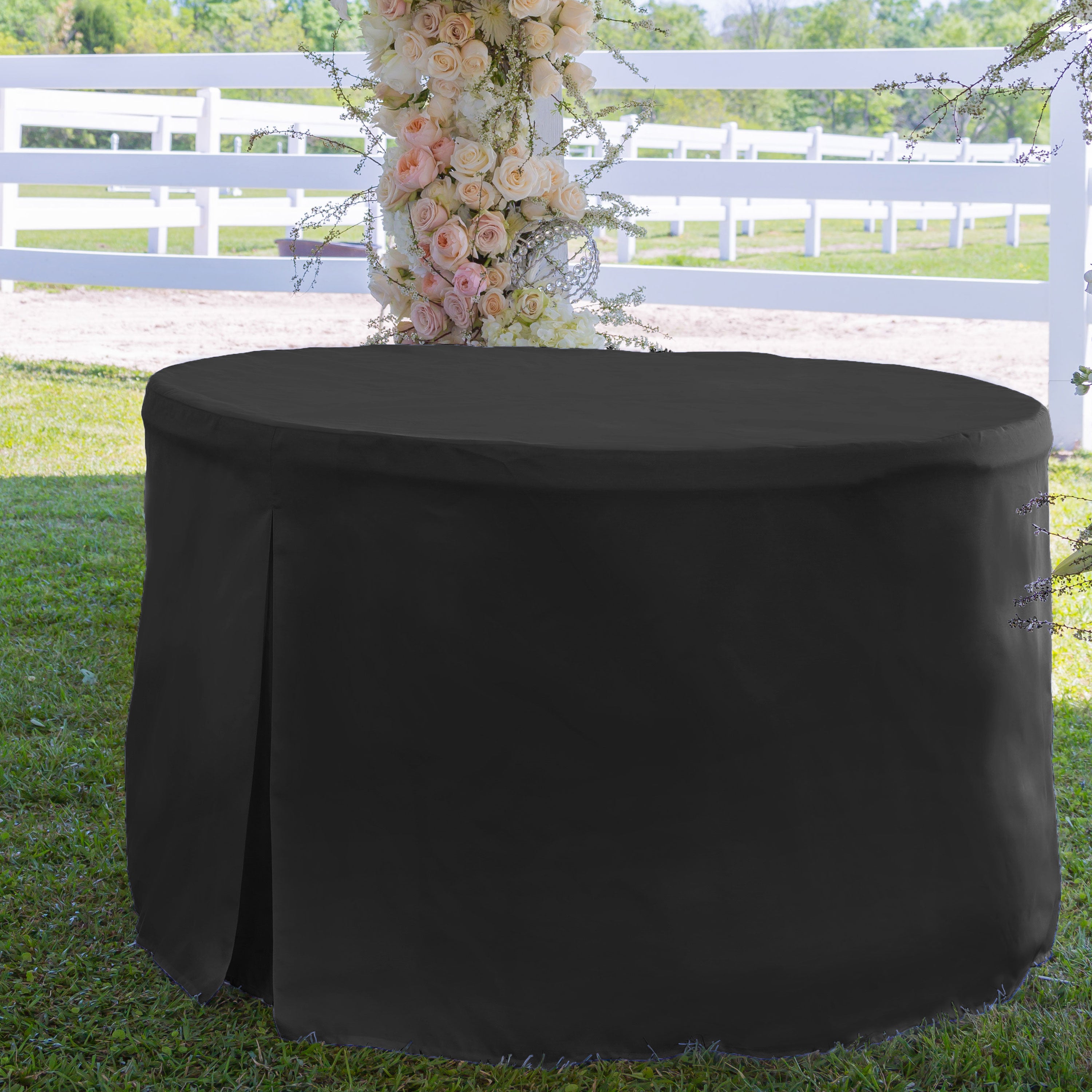 Black round table cover draped over a 60-inch table, set on grass with a floral backdrop.