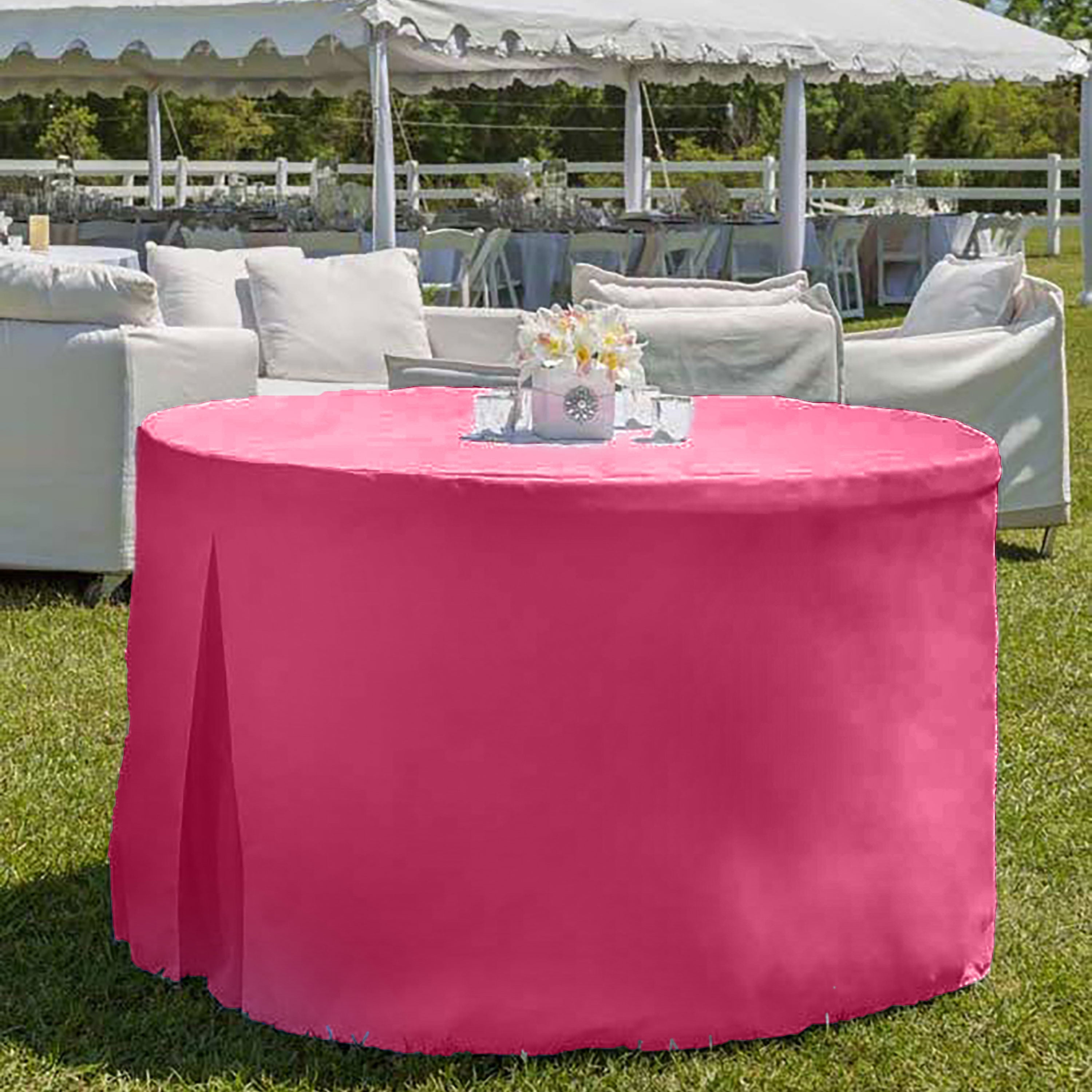 Round table covered with a pink tablecloth, set outdoors with a floral centerpiece and seating in the background.