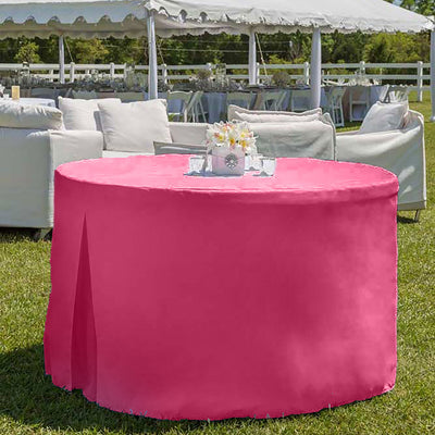 Round table covered with a pink tablecloth, set outdoors with a floral centerpiece and seating in the background.