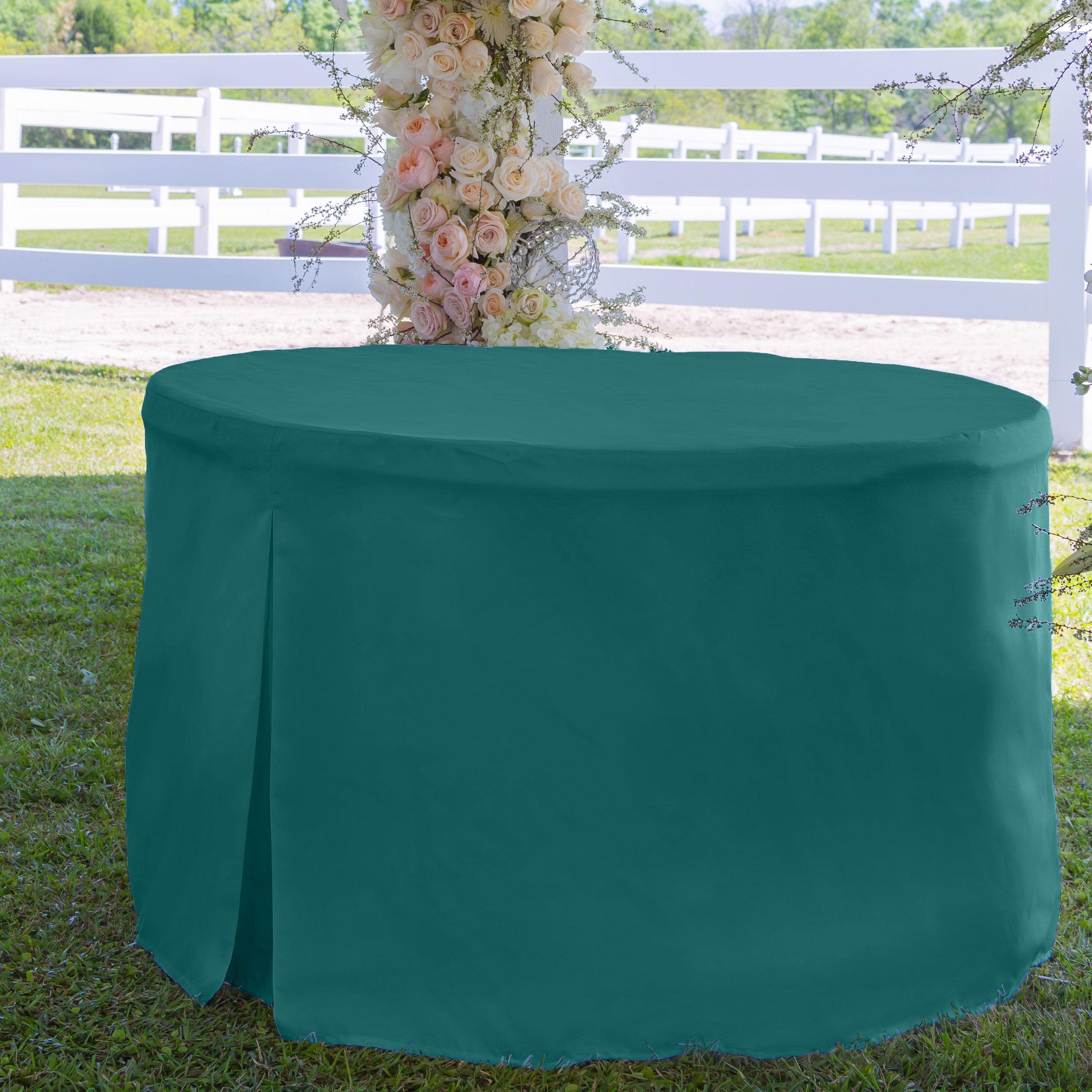 Round table cover in teal, designed to fit a 60-inch table, with a draped edge on a grassy outdoor setting.