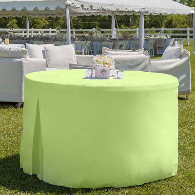 Round table covered with a light green tablecloth, set outdoors with a floral centerpiece and seating in the background.