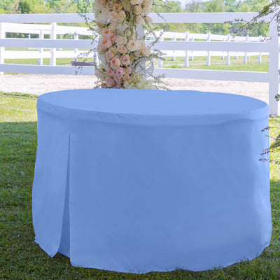 Round table covered with a light blue tablecloth, set on grass with a floral arrangement in the background.