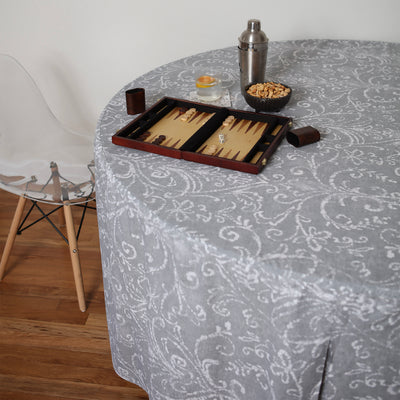 Round table covered with a gray patterned tablecloth, featuring a backgammon set, snacks, and a cocktail shaker.