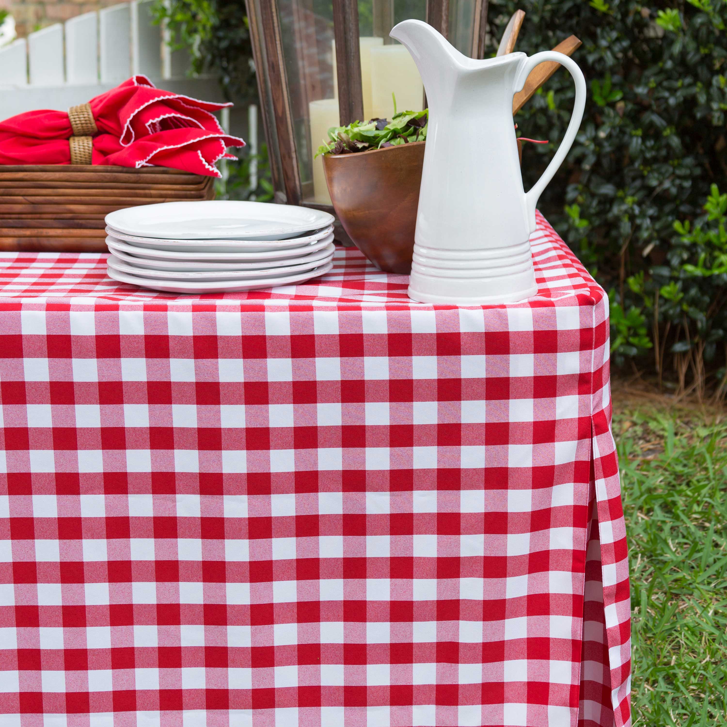 Red and white checkered table cover draped over a table with plates, a pitcher, and a bowl of salad.