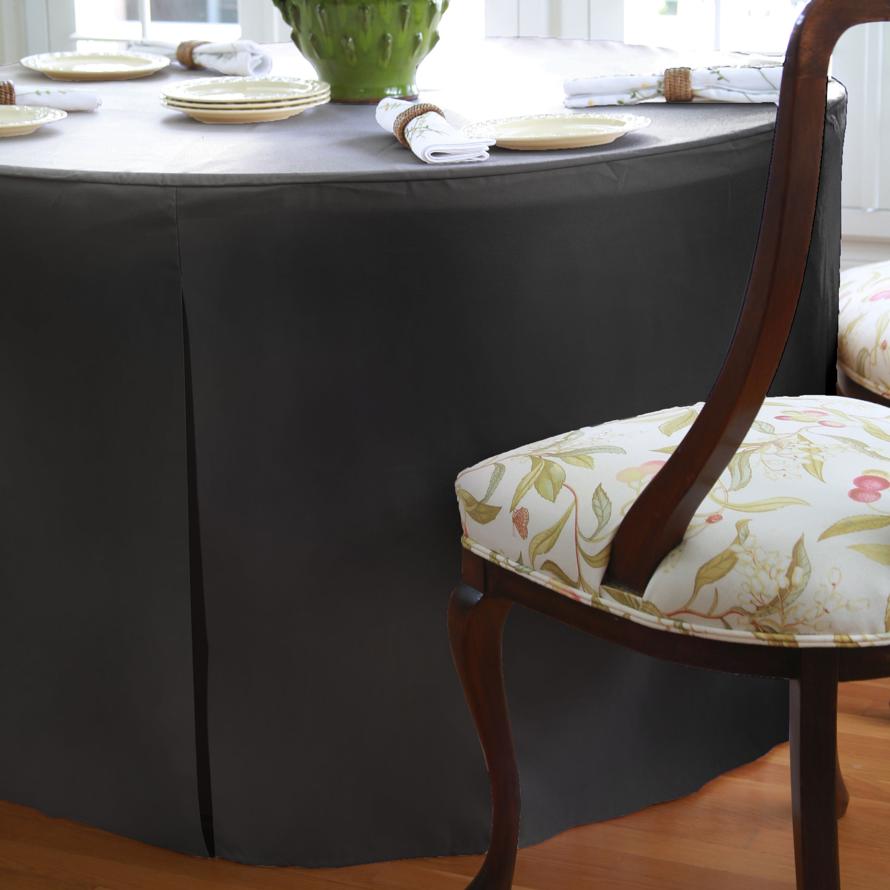 Round black table cover drapes over a 60-inch table with a floral chair visible beside it.