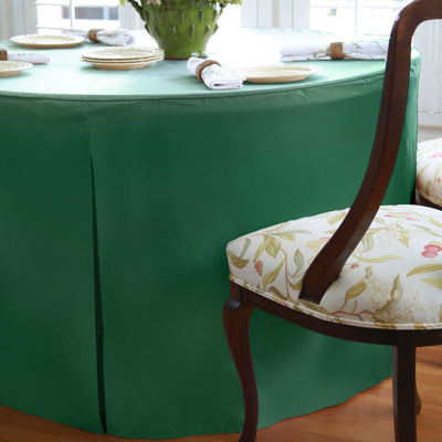 Green round table cover drapes over a 60-inch table, with floral-patterned chair visible beside it.