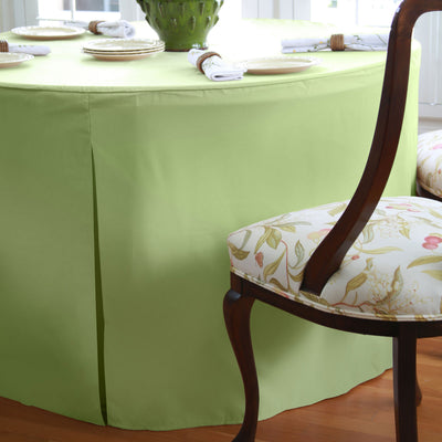 Round table covered with a light green tablecloth, with decorative plates and napkins on top, and a chair with floral upholst
