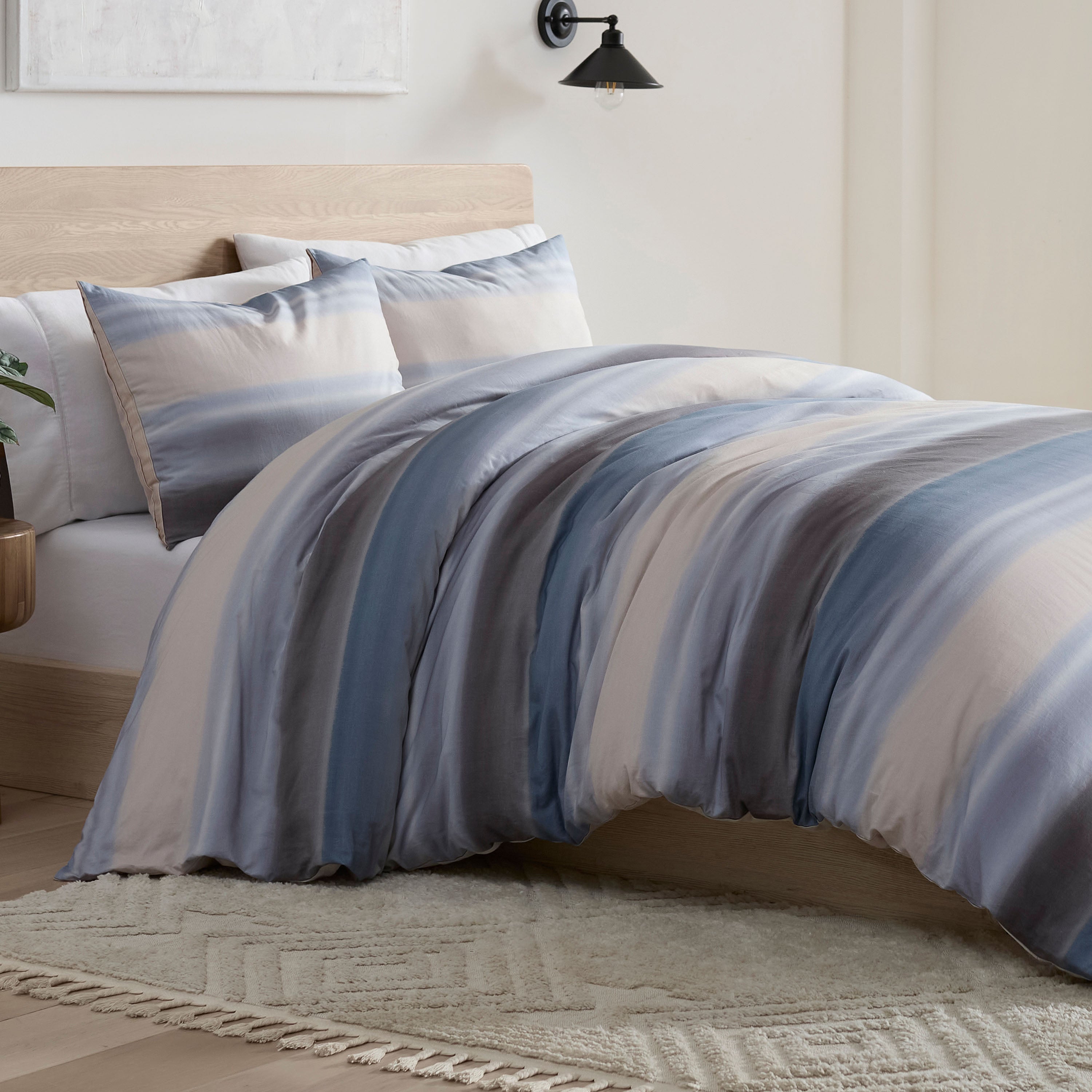 Comforter set featuring blue and beige stripes, with matching pillow shams, placed on a bed with a wooden headboard.