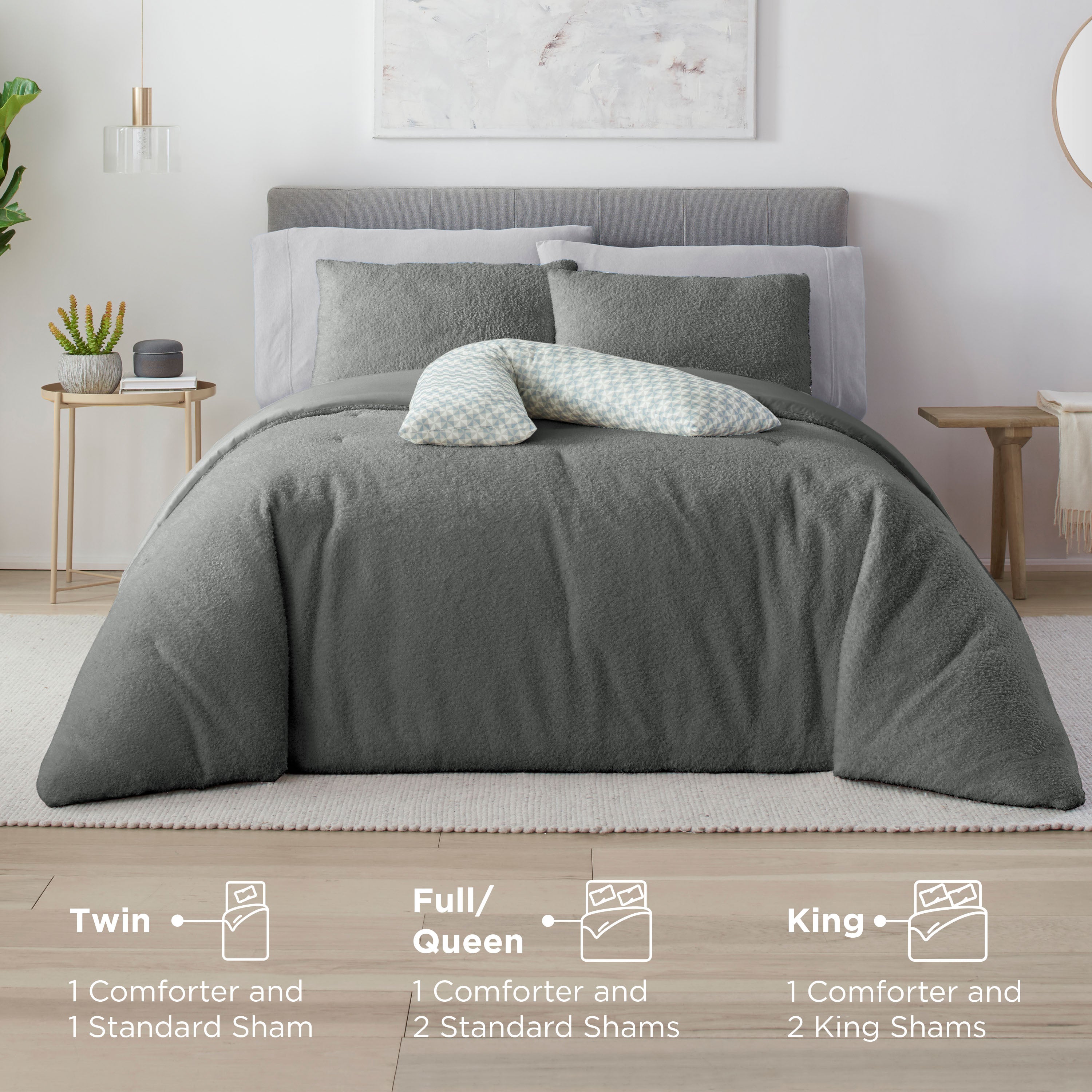 Gray comforter set on a bed with two standard shams and a decorative pillow, alongside a nightstand with plants.