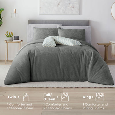 Gray comforter set on a bed with two standard shams and a decorative pillow, alongside a nightstand with plants.