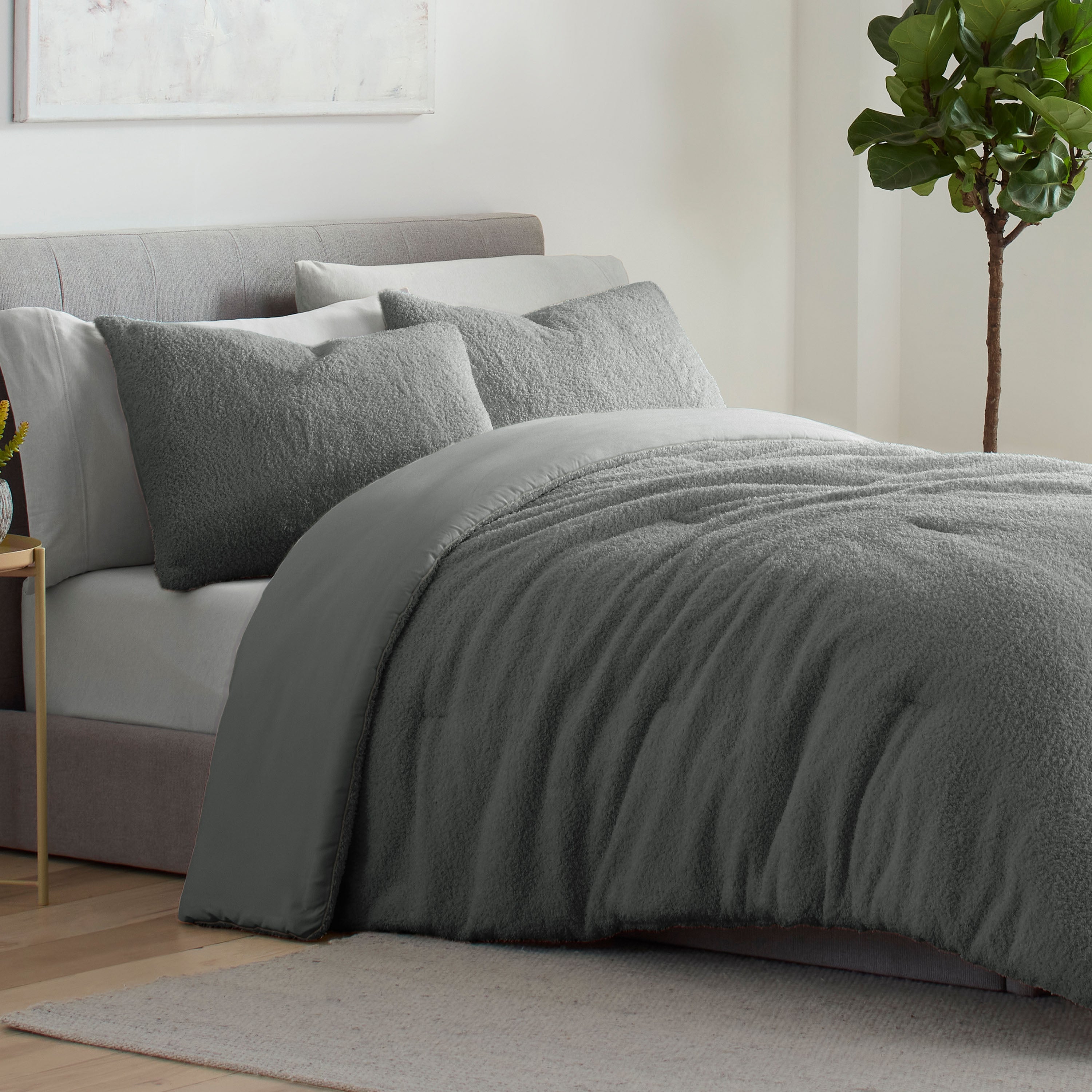 Gray comforter set with textured surface and matching pillows on a bed, accompanied by a small plant in the background.