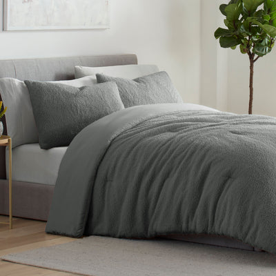 Gray comforter set with textured surface and matching pillows on a bed, accompanied by a small plant in the background.