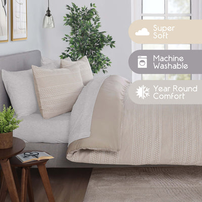 Comforter set on a bed with decorative pillows, a plant, and a side table with glasses and a book.
