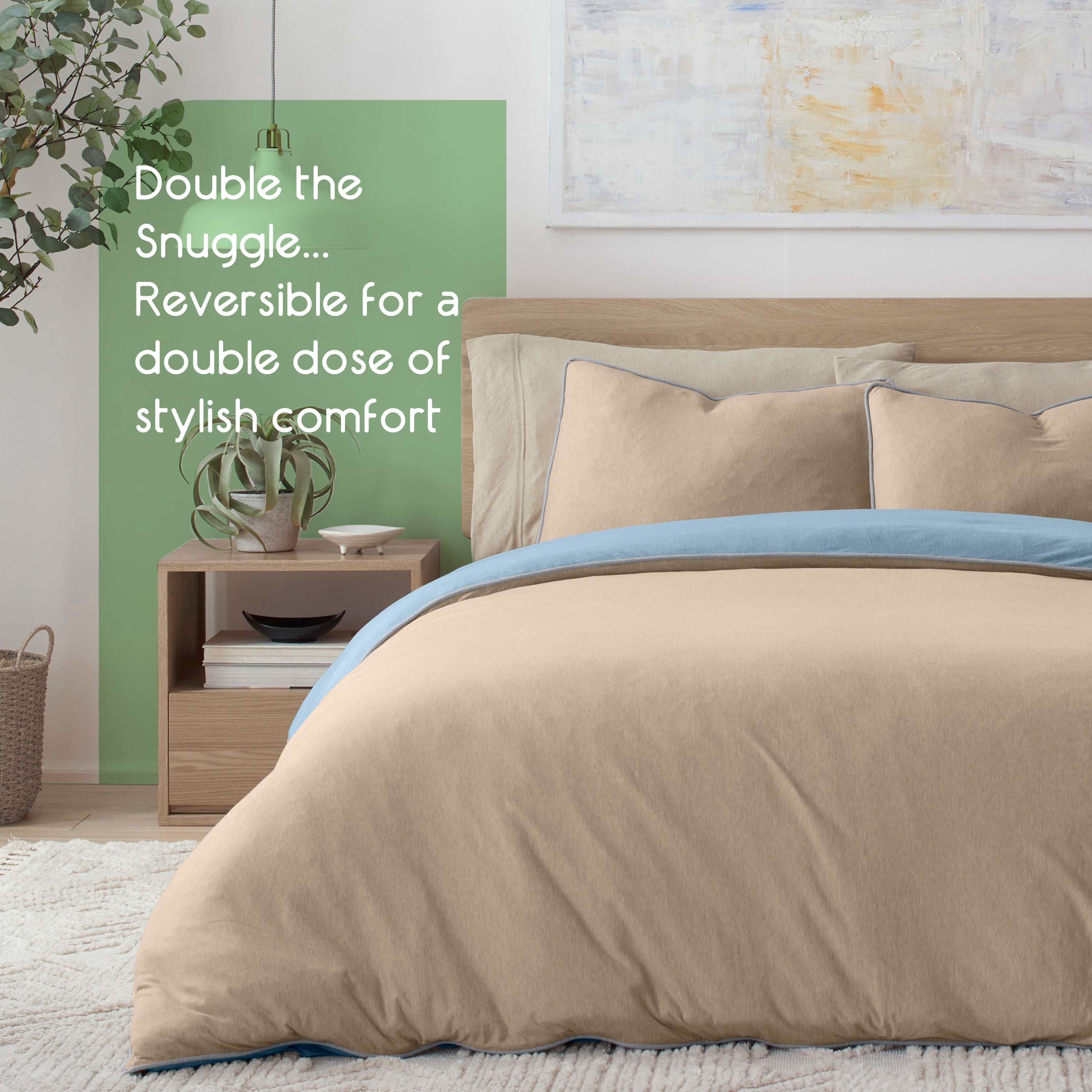 Reversible comforter set in beige and blue with matching pillows on a bed, alongside a nightstand and plant.