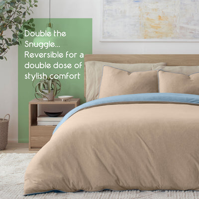 Reversible comforter set in beige and blue with matching pillows on a bed, alongside a nightstand and plant.