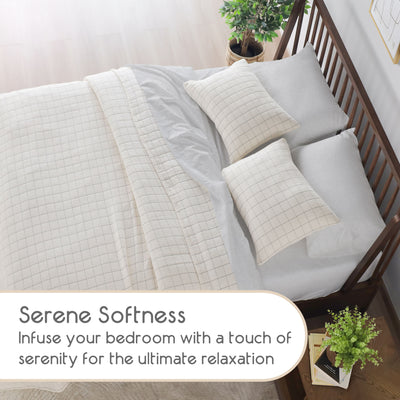 Coverlet set featuring a grid pattern, with decorative pillows and a plant on a wooden bed frame.