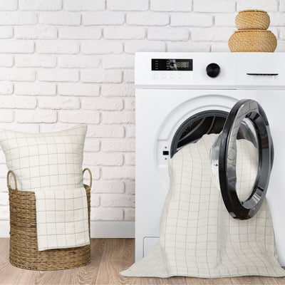A cream coverlet and pillow are placed near a washing machine in a laundry setting.