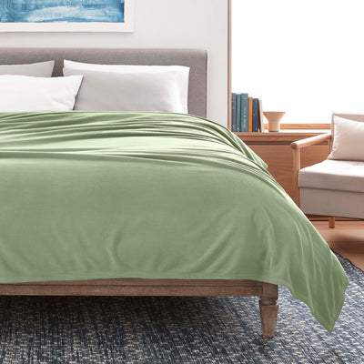 Light green micro fleece blanket draped over a bed with gray headboard and white pillows, in a modern room setting.