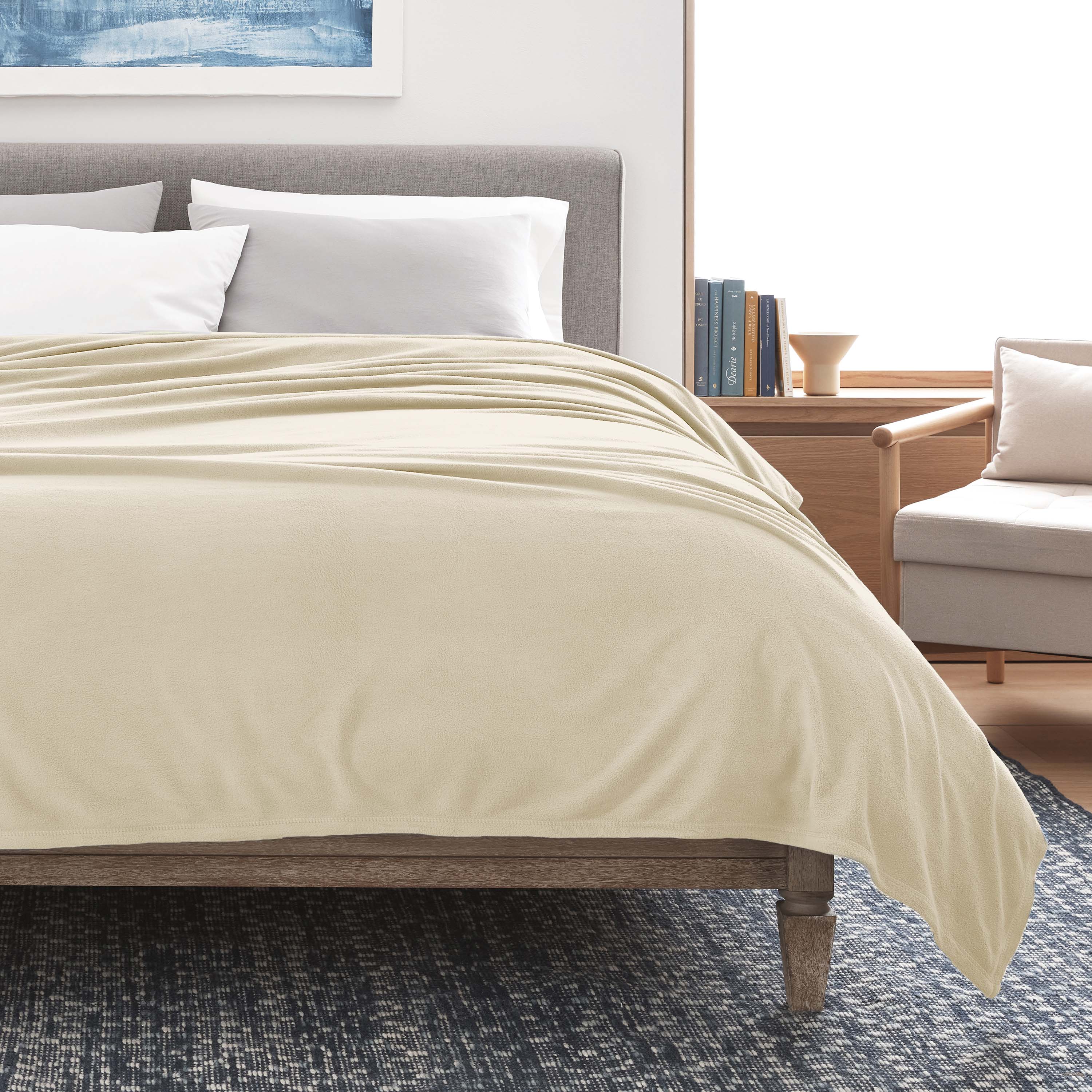 Beige micro fleece blanket draped over a bed with white pillows and a wooden frame, set in a modern room.