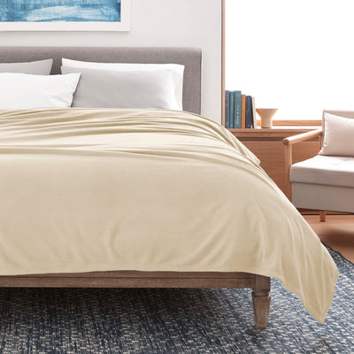 Beige micro fleece blanket draped over a bed with white pillows and a wooden frame, set in a modern room.