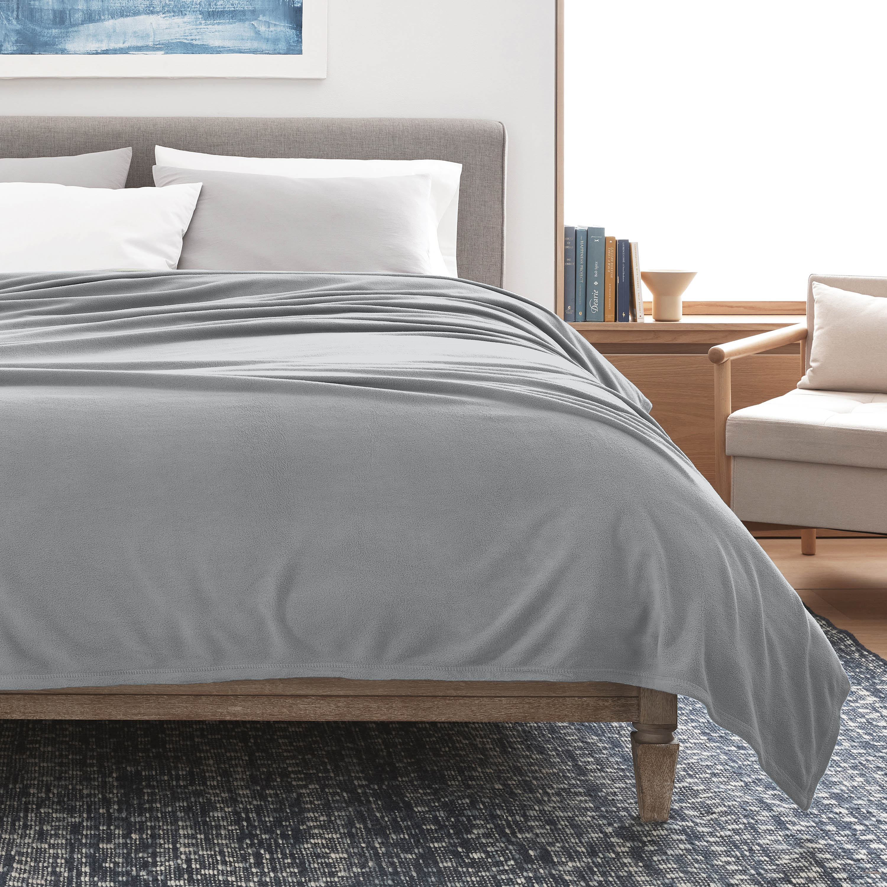 Gray microfleece blanket draped over a bed with white pillows, set in a modern room with a chair and bookshelf.