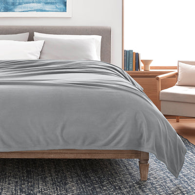Gray microfleece blanket draped over a bed with white pillows, set in a modern room with a chair and bookshelf.