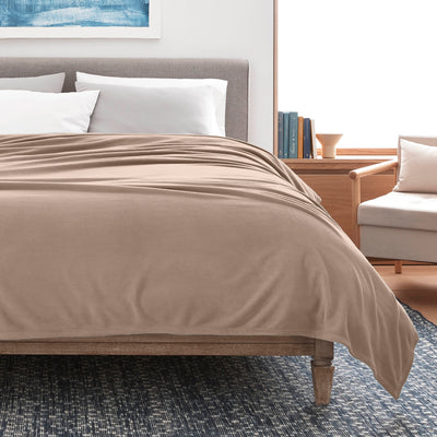 Tan microfleece blanket draped over a bed with white pillows, set in a modern room with wooden furniture.