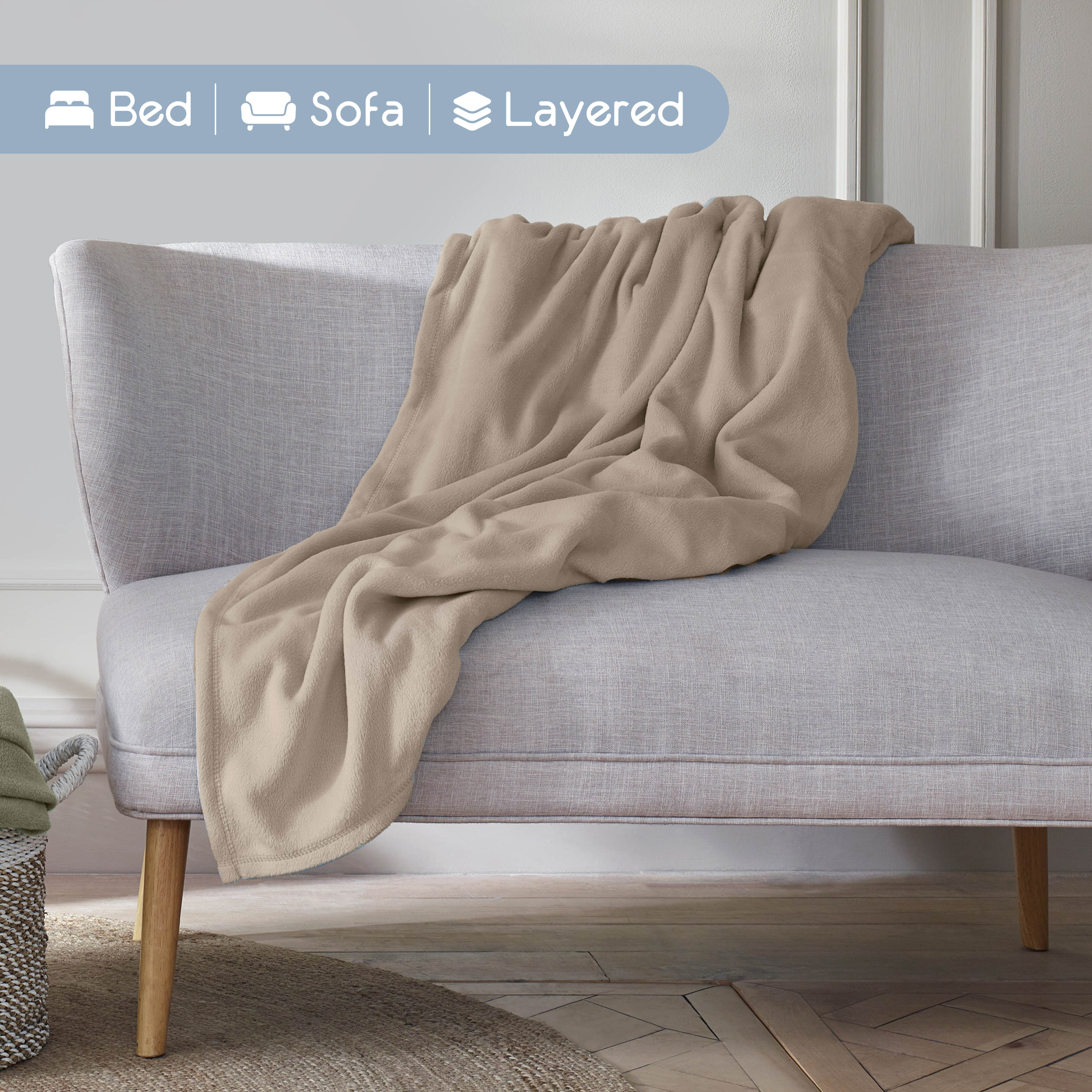 A beige microfleece blanket is draped over a light gray sofa in a cozy living space.